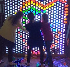 three girls are standing in front of a colorful wall with circles on it and lights behind them