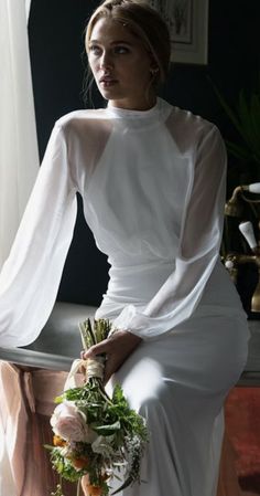 a woman in a white dress sitting on a table with flowers and greenery next to her