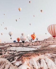 many hot air balloons are flying in the sky over some mountains and deserts, with snow on the ground