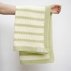 a hand holding a green and white crocheted blanket