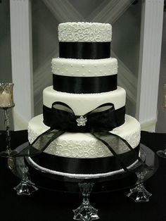 a three tiered wedding cake with black and white ribbons on the top, sitting on a table