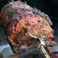 a large piece of meat is being cooked on an outdoor grill with tongs in it