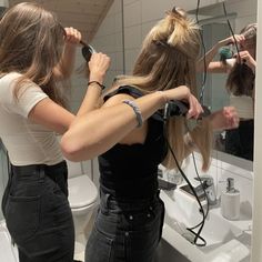 two women blow drying their hair in front of a mirror while another woman brushes her hair