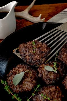 some meat patties in a black pan with herbs on the side and a fork next to it