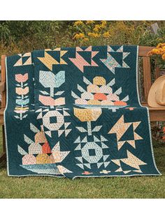 a quilt on a wooden bench with flowers in the back ground and a hat sitting on top of it