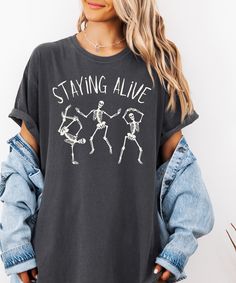 Get into the groove this Halloween with our "Staying Alive" shirt, featuring three funky dancing skeletons that bring the spooky and the fun! This Halloween shirt is perfect for those who love to mix humor with their festive spirit, showing that even skeletons can keep the beat alive. The playful design is a nod to the classics, making it a standout skeleton lover tee that's both trendy and timeless. Whether you're sipping on your morning brew or heading out to a Halloween party, this shirt pair Skeleton Mom Shirt, Pumpkin Funny, Funny Skull, Skeleton Pumpkin, Dancing Skeletons, Dancing Skeleton, Funny Skeleton, Skeleton Halloween, Skeleton Shirt