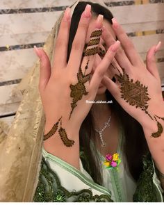 a woman is covering her face with her hands while wearing henna designs on her hand