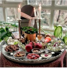 a table topped with lots of food next to two candles and flowers in front of a window