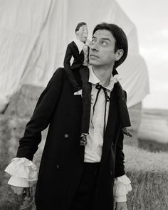 a black and white photo of a man with a doll on his shoulder, standing in front of a hay bale