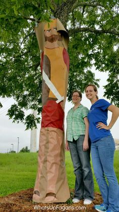 two people standing in front of a tree with paper mache on it's trunk