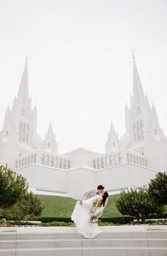 a bride and groom kissing in front of a large white building with spires on it