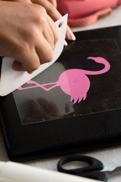 someone is using a pink flamingo stencil on a black cutting board with scissors