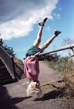 a person doing a handstand on the side of a metal rail near some stairs