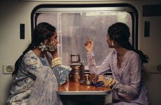 two women sitting at a table in front of a window with rain falling on them