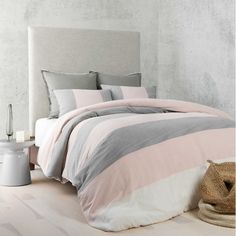 a bed with pink and grey comforters in a white room next to a lamp