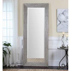 a large mirror sitting on top of a wooden floor next to a vase and table