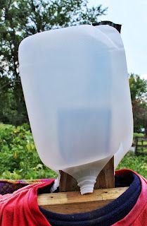 a plastic jug sitting on top of a wooden stand in front of some grass and trees