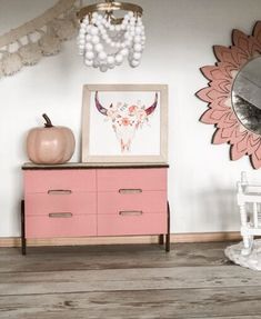 a pink dresser in a room with a mirror and decor on the wall above it