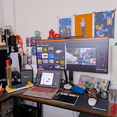 a desk with two computer monitors and a laptop on it in front of a wall full of pictures