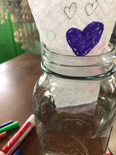 a jar with some writing on it sitting on a table next to crayons