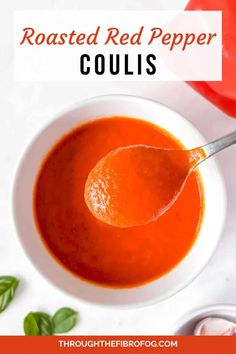 a bowl of roasted red pepper coulis with a spoon in it and basil on the side