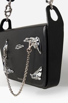 This shoulder bag from Published By combines leather construction with the brand's penchant for dynamic shapes and structure. It has their signature silver-tone ornamentation at the front, completed with a mini silver chain and an oversized leather shoulder strap held by wavy chain clasps. Silver Leather Shoulder Bag With Hardware, Modern Evening Bag With Hardware Details, Modern Evening Bag With Hardware, Modern Evening Bags With Hardware, Silver Top Handle Shoulder Bag With Gunmetal Hardware, Designer Shoulder Bag With Hardware For Evening, Leather Shoulder Bag With Hardware For Evening, Evening Leather Shoulder Bag With Hardware, Elegant Crossbody Shoulder Bag With Hardware