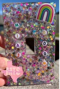 someone is holding up a light switch plate that has letters on it and rainbows in the background