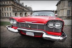 an old red car parked in front of a large building