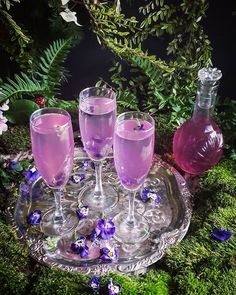 three wine glasses on a tray with purple flowers and greenery in the back ground