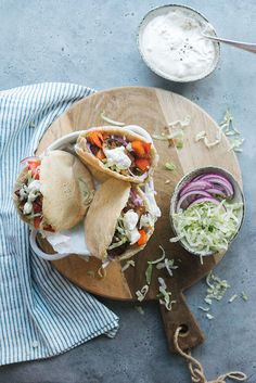 two pita sandwiches sitting on top of a wooden cutting board next to a bowl of coleslaw