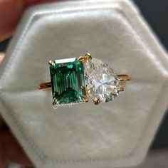 an emerald and diamond ring sitting on top of a white velvet bag with a gold band