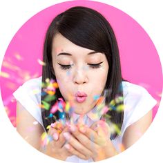 a young woman blowing confetti on her fingers while looking at the camera with pink background