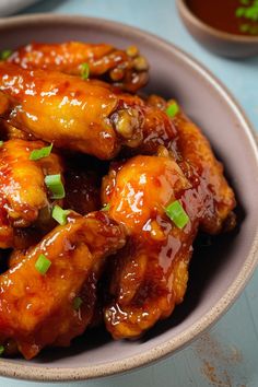 a bowl filled with chicken wings covered in sauce and garnished with green onions