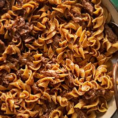 a bowl filled with pasta and beef on top of a green table next to a spoon