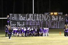 a group of people standing on top of a field holding up a sign that says tell your girlfriends you're friday night