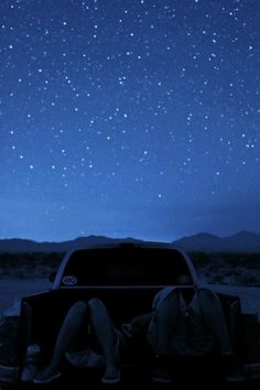 a woman sitting in the back of a pick up truck under a night sky filled with stars