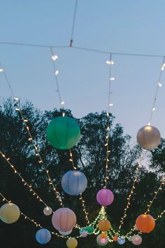 paper lanterns hanging from string lights in front of trees