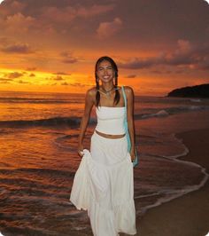 a woman standing on top of a sandy beach next to the ocean at sunset or dawn