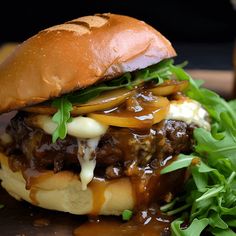 a hamburger with meat, cheese and onions on it sitting on a cutting board next to some greens