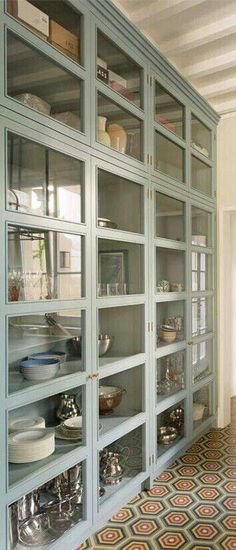 a large glass cabinet with many dishes on it's shelves in a room that is painted blue