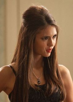 a woman with long brown hair wearing a black top and necklace standing in front of a mirror