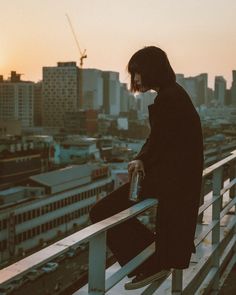 a man sitting on top of a metal railing next to a tall cityscape