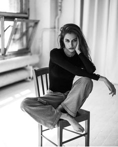 a black and white photo of a woman sitting on a chair with her hands behind her head