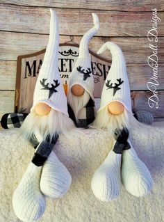 two white and black knitted gnomes sitting on top of a blanket next to a wooden sign