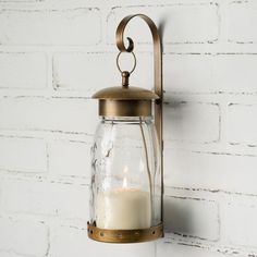 a candle is lit in a glass jar hanging on a brick wall with a metal bracket