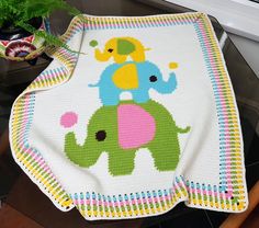 an elephant crocheted blanket on top of a wooden table next to a potted plant