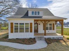 a small white house with a porch and covered in wood shingles on the roof