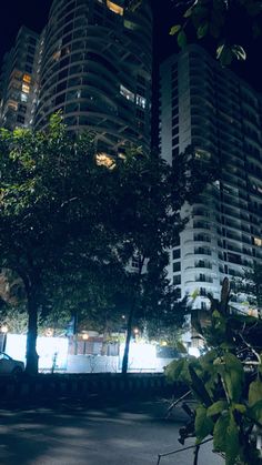 a man riding a skateboard at night in front of high rise buildings and trees