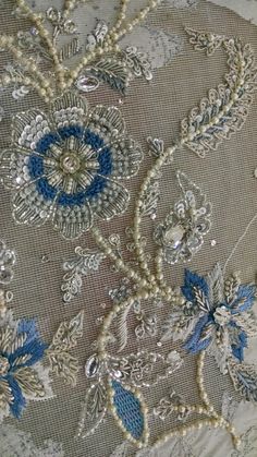 an embroidered fabric with blue flowers and pearls on the bottom is seen in this close up photo