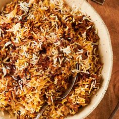 a white bowl filled with rice and meat on top of a wooden table next to utensils